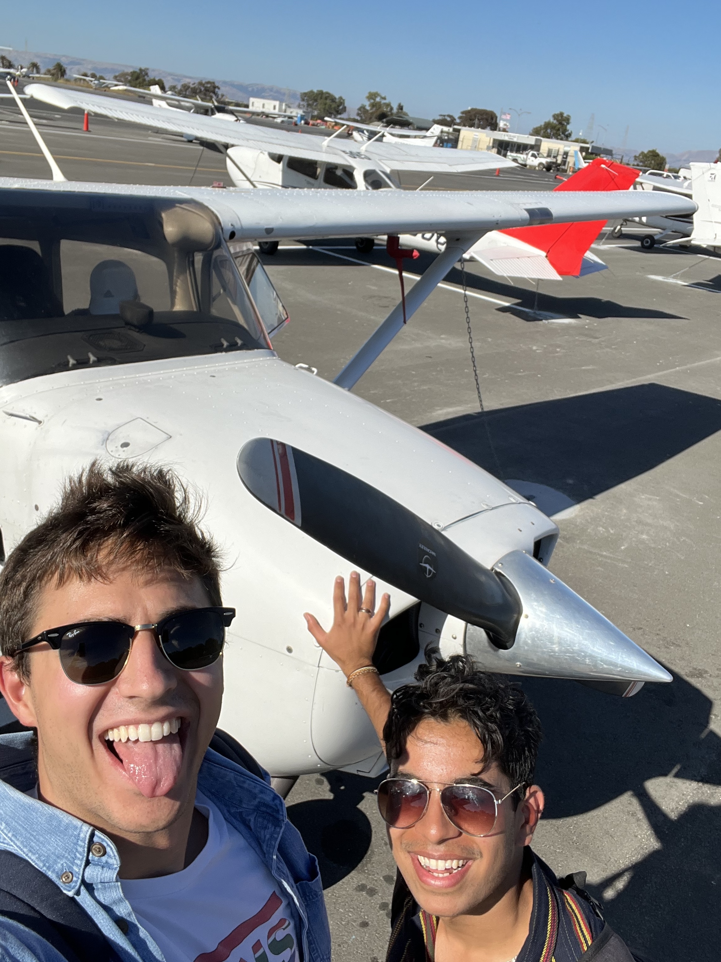 John and Dhruv outside of their Cessna 172 Skyhawk for the day. John appears to be checking for wind using his tongue. Sensory augmentation is pervasive.